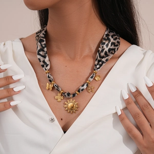 Detail of leopard print silk scarf necklace with golden sun and cross charms on model