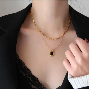 Close-up of double-layer gold chain necklace with black rectangular pendant on a model