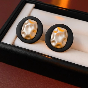 Detail of oval earrings with black matte finish and textured gold center in jewelry box