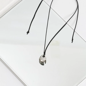Detail of a minimalist silver bean pendant on black cord over a mirror base