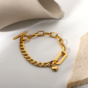 Close-up of golden Cuban link bracelet with heart pendant and toggle clasp on stone