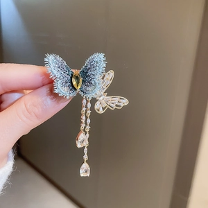 Detail of butterfly brooch featuring blue embroidery, crystal studs and tassel chains