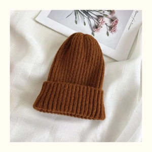 Close-up of caramel brown ribbed knit beanie on white fabric with artistic card detail