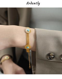 Macro shot of gold mesh bracelet with sunflower charms and blue stones on model