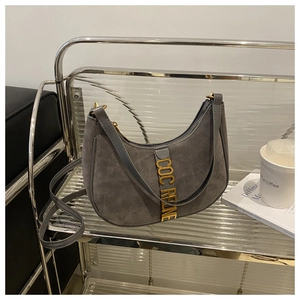 Detailed macro view of dark gray suede underarm bag with gold metal logo and hardware