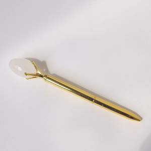 Detailed close-up of golden metal ballpoint pen featuring a translucent crystal gemstone top
