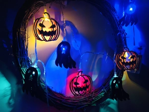 Macro shot of Halloween LED string lights with wooden pumpkin and ghost shapes on a wreath