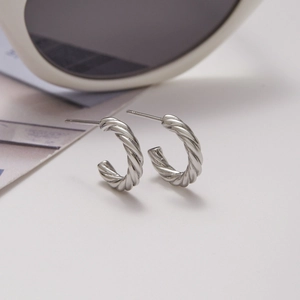 Close-up of silver C-shaped twisted rope earrings with metallic luster on white surface
