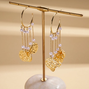 Close-up of golden tassel earrings with hammered texture and small pearls on T-stand