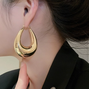 Close-up of a large polished gold teardrop U-shaped hoop earring worn by a model