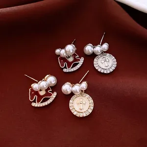 Elegant pearl drop earrings with rocking horse and cross pendants on red velvet background