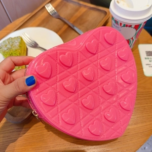 Pink heart-shaped silicone crossbody bag with embossed patterns shown in a cafe setting