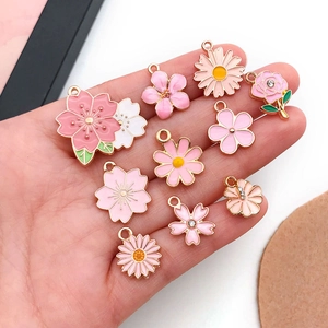 Pink enamel flower charms for DIY jewelry held in hand showing cherry blossom details