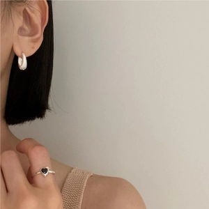 Detail view of a textured silver hoop earring and a thin ring with a black heart charm