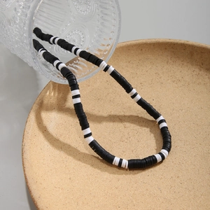 Minimalist black and white polymer clay beaded necklace cascading over a glass and plate