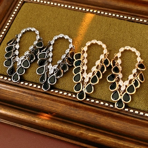 Close-up of gold and silver drop earrings with black pear gems on green fabric
