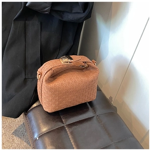 Detailed view of brown woven texture handbag with golden metal lock on a dark stool