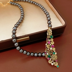 Vue détaillée du pendentif doré vintage avec gemmes sur un collier de perles gris foncé