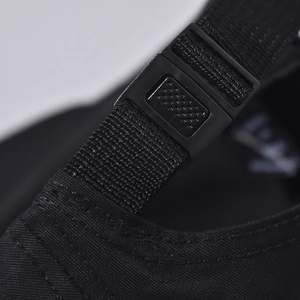 Close-up of the adjustable plastic buckle and nylon strap on the black baseball cap