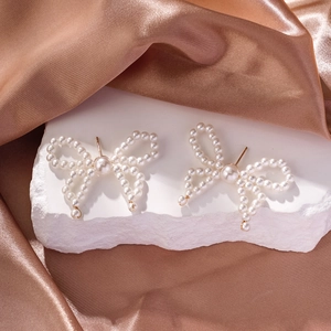 Detailed view of pearl bow earrings on white rock and elegant brown silk background