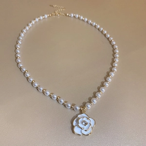 Detail of elegant pearl necklace with white enamel camellia flower and gold finish