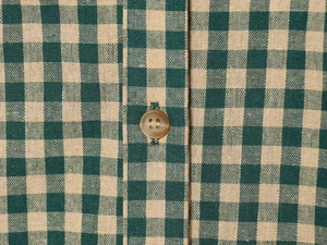 Detailed macro view of green and yellow plaid shirt fabric with a brown button