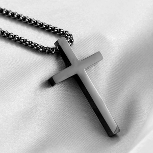 Gros plan du pendentif croix en métal noir sur chaîne box et fond de satin gris