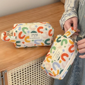 Macro view of cream quilted makeup bag with colorful C-prints and soft hand strap