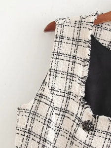 Close-up of black and white tweed vest fabric with fringe trim and decorative button