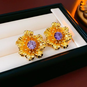 Detailed shot of vintage gold flower earring with a purple zircon stone on a beige cushion