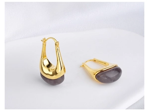 Macro detail of U-shaped gold earrings with translucent lavender resin on white fabric