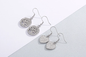 Detailed view of silver hollow tree of life and sparkling heart-shaped drop earrings