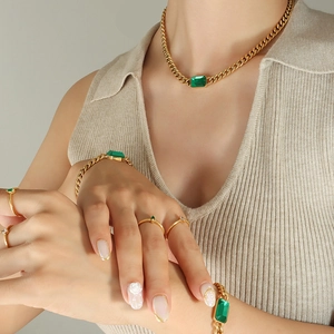 Golden chunky Cuban chain set with emerald green stones and minimalist rings on model