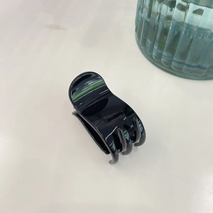 Détail d'une pince à cheveux noire pour queue de cheval sur une table crème épurée