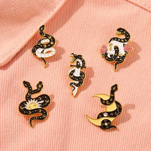 Gothic snake and skull enamel pins set with celestial motifs on pink denim fabric