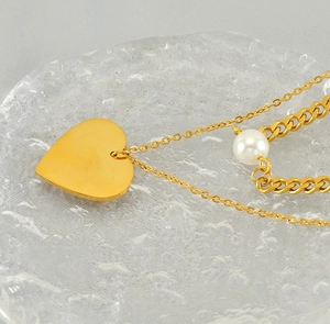 Macro detail of a double-layered gold heart necklace with pearl on a glass tray