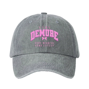 Grey washed denim baseball cap with pink Demure text and bow print on a white background