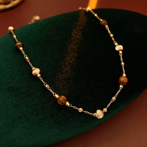 Dettaglio della collana placcata in oro con perle occhio di tigre su velluto verde