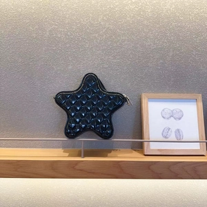Detail of a black star-shaped quilted handbag with glossy finish on a wooden shelf