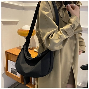 Detail of black nylon crescent bag with adjustable strap worn by model in cozy interior