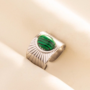 Macro shot of wide stainless steel ring with green malachite stone on beige fabric