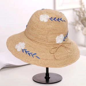 Detailed embroidery of white fabric flowers and navy stitching on raffia sun hat