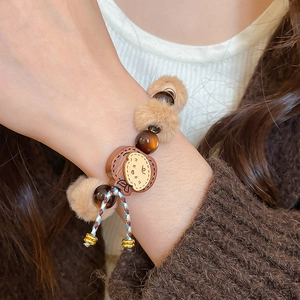 Détail d'un bracelet en perles avec pompon en peluche et breloque ours en bois au poignet