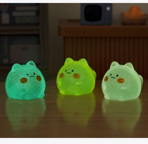 Luminous cat-shaped resin figurines glowing in the dark on a wooden surface