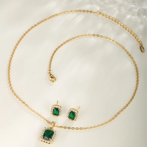 Elegant gold jewelry set with square green stones and cubic zirconia on beige background