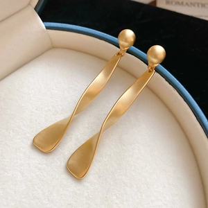Gros plan de boucles d'oreilles pendantes torsadées en or mat avec perles métalliques