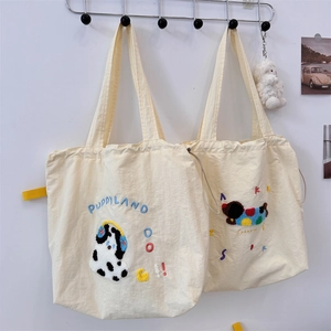Detail of cream drawstring tote bags with puppy embroidery and tufted lettering