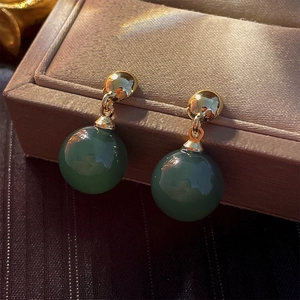 Detailed view of vintage green spherical drop earrings on a brown textured jewelry box edge