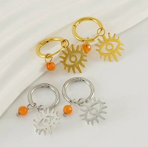 Detailed shot of gold and silver evil eye hoop earrings with orange beads on white fabric