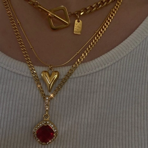 Close-up of layered gold heart pendant necklaces with OT toggle clasp and red gemstone